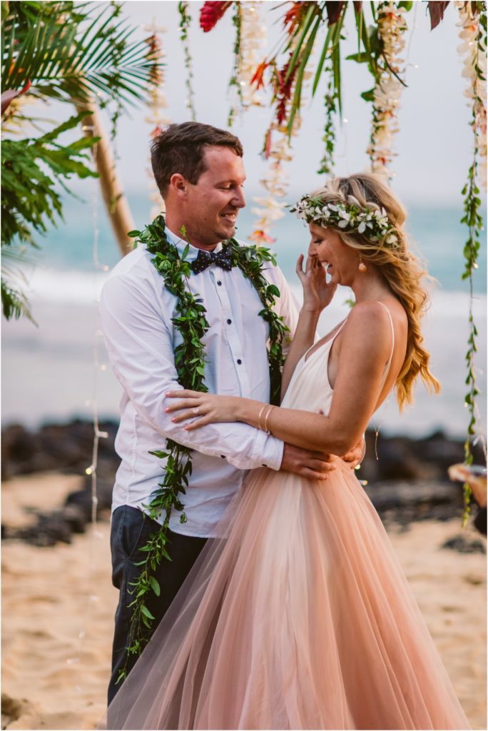 bride and groom under homemade flower arch at dream beach wedding kauai hawaii pink dress